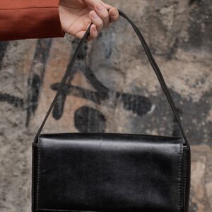 Close-up of a hand holding a stylish black handbag with a graffiti-covered wall background.