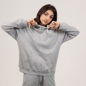 Serious female wearing oversize hoodie and sweatpants standing against white background and looking at camera